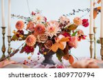 Beautiful flower composition with autumn orange and red flowers and berries. Autumn bouquet in vintage vase on a wooden table with pink tissue and candles