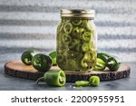 Small photo of Jar of homegrown quick pickled homegrown jalapeno peppers surrounded by fresh green jalapeno peppers on a wooden cutting board