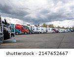 Small photo of Industrial standard different bigs rigs semi trucks tractors with loaded semi trailers standing for break and truck driver rest on the wide truck stop parking lot according to the traffic schedule