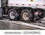 Experienced truck driver puts chains on the wheels of the big rig semi truck with semi trailer to drive safely on a winter highway during a snow storm in the Lake Shasta region in California