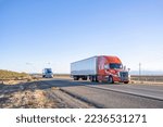 Industrial long hauler big rigs semi trucks team transporting commercial cargo in loaded dry van semi trailers running together on the flat straight highway road in California