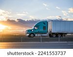 Industrial long hauler big rig green semi truck tractor with chrome parts transporting commercial cargo in loaded dry van semi trailer running on the highway road at sunset time in California