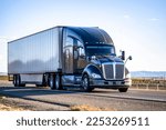 Small photo of Industrial long hauler big rig black semi truck tractor with truck driver sleeping compartment transporting cargo in dry van semi trailer driving on the straight wide highway road in California