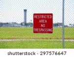 A RESTRICTED AREA NO TRESPASSING sign on a fence at an airport with the air traffic control tower in the background