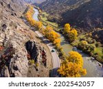From above drone view of van driving on curvy asphalt road near fast river and autumn trees on sunny day in mountainous terrain