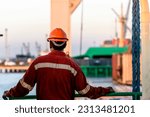 Small photo of Seaman in red working overall and orange helmet on deck. Working at sea. Cargo vessel. Mooring operations. Able seaman.