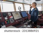 Officer on watch with radio on the navigational bridge. Caucasian man in blue uniform sweater on the bridge of cargo ship.