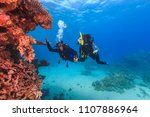 Explorer people underwater . Two adult person diving in first time on tropical reef with blue background, beautiful coral and small fish. Man pointing on top and holding woman by hand.