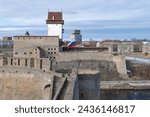 Small photo of Russian flag in the Ivangorod fortress against the background of Hermann's Castle (Narva, Estonia) on a March day. Border between Russia and Estonia