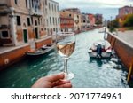 White wine glass for tasting during walking in Venice. Water canals and embankments with bar and restaurants of famous italian city.