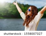 Beautiful smiling female model enjoying freedom with hands raised. Woman in sunglasses outdoor fashion portrait. Close up