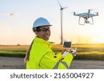 Happy Female Operator inspecting Wind turbine with drone at sunset. Drone inspection concept image. renewable energy wind park in europe