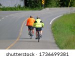 Two cyclists wear bright, reflective clothing on a two lane road to create high visibility awareness for motorists. 