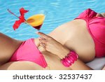 Woman in a bikini with a cocktail by a blue swimming pool