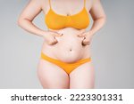 Fat woman in orange underwear on gray background, overweight female body, body positive concept