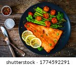Fried salmon fillet with asparagus and cherry tomatoes served on black plate on wooden table