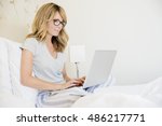 Shot of mature woman sitting in bed and using her laptop while working online. 