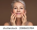 Small photo of Portrait of gorgeous happy mature woman, senior older 60 year lady looking at camera touching her face