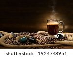Cup glass of coffee with smoke and coffee beans and coffee capsules on burlap sack on old wooden background