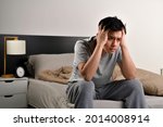 Small photo of Depressed young Asian man sitting in bed cannot sleep from insomnia