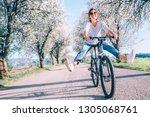 Happy smiling woman cheerfully spreads legs on bicycle on the country road under blossom trees. Spring is comming concept image.