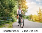 Small photo of Portrait of a happy smiling man dressed in cycling clothes, helmet and sunglasses riding a bicycle on the asphalt out-of-town bicycle path. Active sporty people concept image.