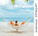 Small photo of Young woman relaxing in wicker hammock on the sandy beach on Mauritius coast and enjoying wide ocean view waves. Exotic countries vacation and mental health concept image.
