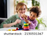Small photo of Mother looking at a child playing with an educational didactic toy. Preschool teacher with a child playing with didactic toys