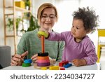 Small photo of Mother looking at a child playing with an educational didactic toy. Young woman and child playing with didactic toys