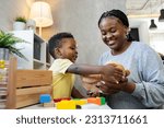 Small photo of A cute little African child plays with colorful didactic educational toys. His proud mother supports him. Kindergarten teacher with child.