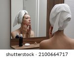 Small photo of Portrait of a beautiful young woman standing in the bathroom and examining her face in the mirror, problematic acne-prone skin concept