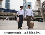 Small photo of Portrait of Handsome professional Burmese or Myanmar businessmen with longyi traditional dress pull luggage in Modern city. Smart guys business trip in Bangkok. Work and travel in Foreign country
