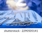 Small photo of A medical or surgical instrument for surgery inside the operating theatre with blur team of doctors in blue gown background.Surgical clamps for a surgeon on the blue tray.Blur background with light.