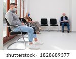 Young and old people with face masks keeping social distance in a waiting room of a hospital or office -  focus on the young man in the foreground