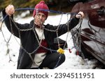 Small photo of Cold and Slippery Road travel Conditions, Adult Caucasian Woman Unhappily Setting Tire Chains in Icy and Unfriendly Winter Conditions on her Car