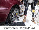 Small photo of Woman Unhappily Setting Tire Chains in Icy and Unfriendly Conditions with Falling Snow