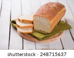 Sliced loaf of homemade  bread on board on white wooden background. Selective focus.
