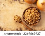 Fried onions in bowl on wooden background with wooden spoon. Crispy fried onions. View from directly above.