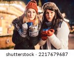 Two women with hot mulled wine in front of Christmas market stand