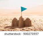 Small photo of Sand castle with a flag on the sea shore.
