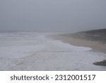 Small photo of Horizontal photo of gloomy turbulent sea, rough waves, a cape covered with forest is visible in the distance. Foamy waves roll along the sandy shore. Evening time. Twilight sky, Portugal, Nazare