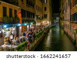 Narrow canal with tables of restaurant in Venice, Italy. Architecture and landmark of Venice. Cozy night cityscape of Venice.