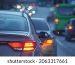 Cars waiting for street light in rush hour traffic jam on dusk busy city street. Shallow DOF, focus on red tail lights.