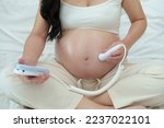 Small photo of close up young pregnant woman using fetal droppler device to listening baby heartbeat