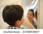 Small photo of A child boy reflected in diverging mirror, spherical mirror creating optical illusion of distorted face and shape on the surface of glass
