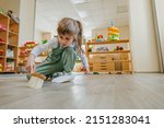 Small photo of Little girl sweeping the floor using a dustpan and a broom at kindergarten