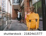 Small photo of Little girl with backpack waving her mother saying goodbye near the school. Back view. Back to school concept.