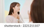 Small photo of unhappy beauty skin care asian woman looking mirror touch and scratch her face with dissatisfaction at home during winter