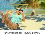 Vacation concept. Enjoying the summer. Young pretty woman in hat and sunglasses using smartphone laying in hammock on the beach.
