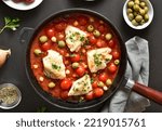 Small photo of Cod stew with chickpeas, cherry tomatoes and olives in skillet over dark stone background. Top view, flat lay